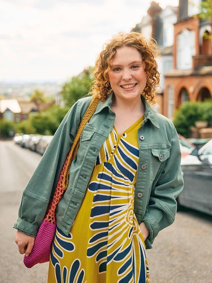 a woman in a yellow dress and green jacket standing on a street